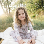 Toddler girl smiling on a blanket in the grass, wearing the Tiny Maps LOTR two-piece pajama set
